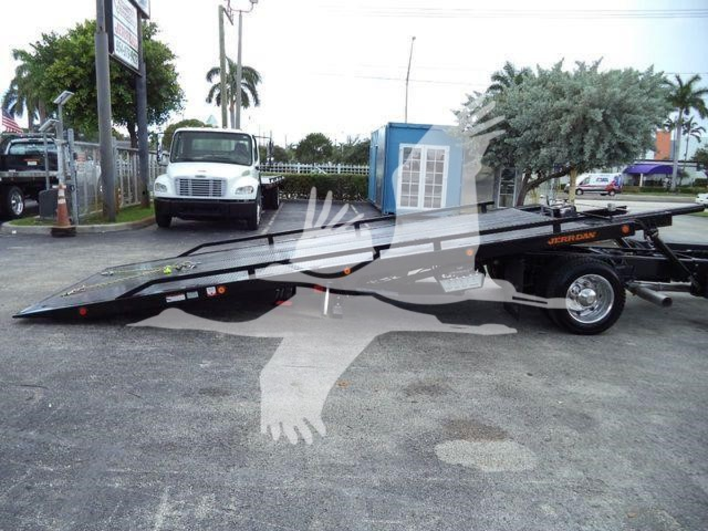 Low-angle view of a 2023 Chevrolet Silverado 6500HD rollback bed equipment trailer in a dealership lot showing long tow deck and wheels.