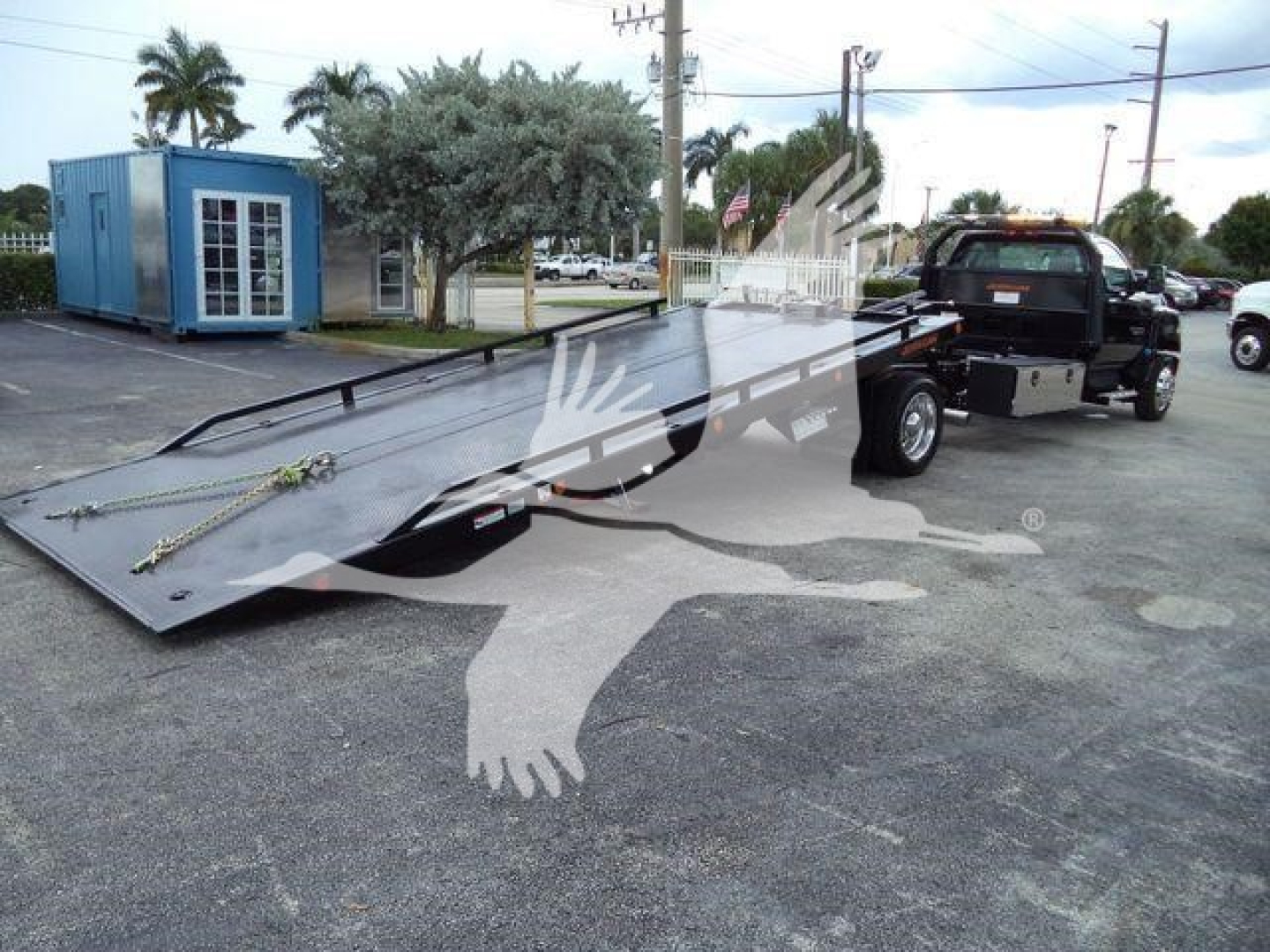 Truck with flatbed rollback trailer in a dealership lot showing a folded heavy-duty ramp and Chevrolet Silverado branding on the trailer.