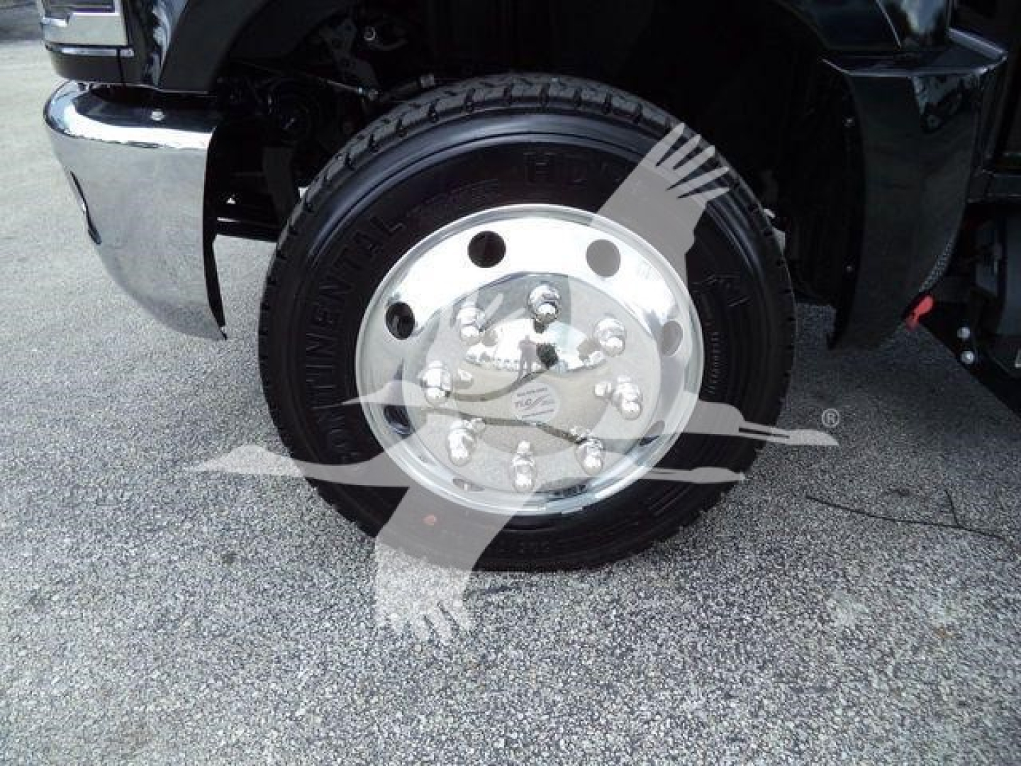 Truck wheel well showing steel wheel with multiple lug nuts and tire, front fender and bumper; faint watermark across image.