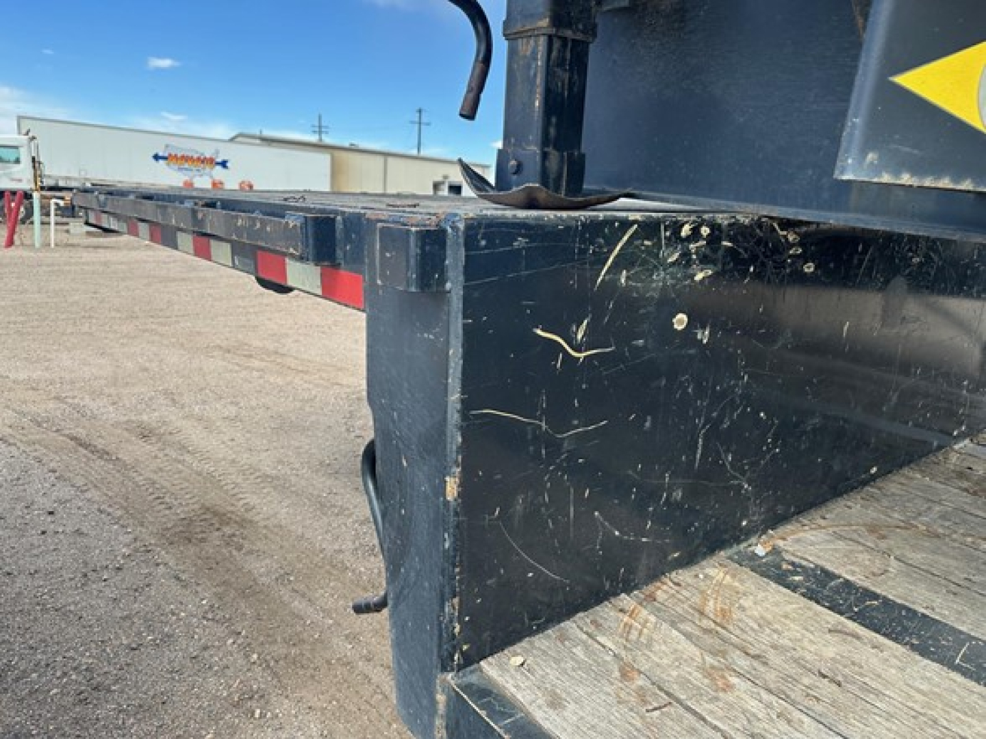 Deck edge of a Great Dane steel spread air drop trailer showing scratched black paint and edge of wooden deck, side rails, and lower corner with a small handle.