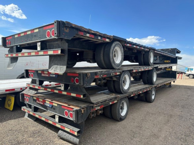 Great Dane steel spread air drop deck trailer stacked on multiple tiers with dual rear axles and wheels visible, black with red and white safety striping.