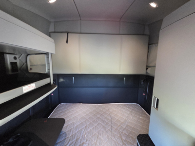 Kenworth T680 sleeper cab interior cargo area with quilted bed, side storage, and overhead compartments. 
