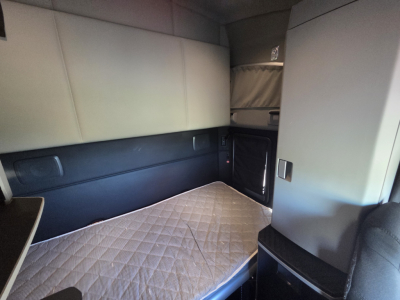 Kenworth T680 sleeper cab interior showing sleeping area with quilted mattress and side storage, dash area not visible.