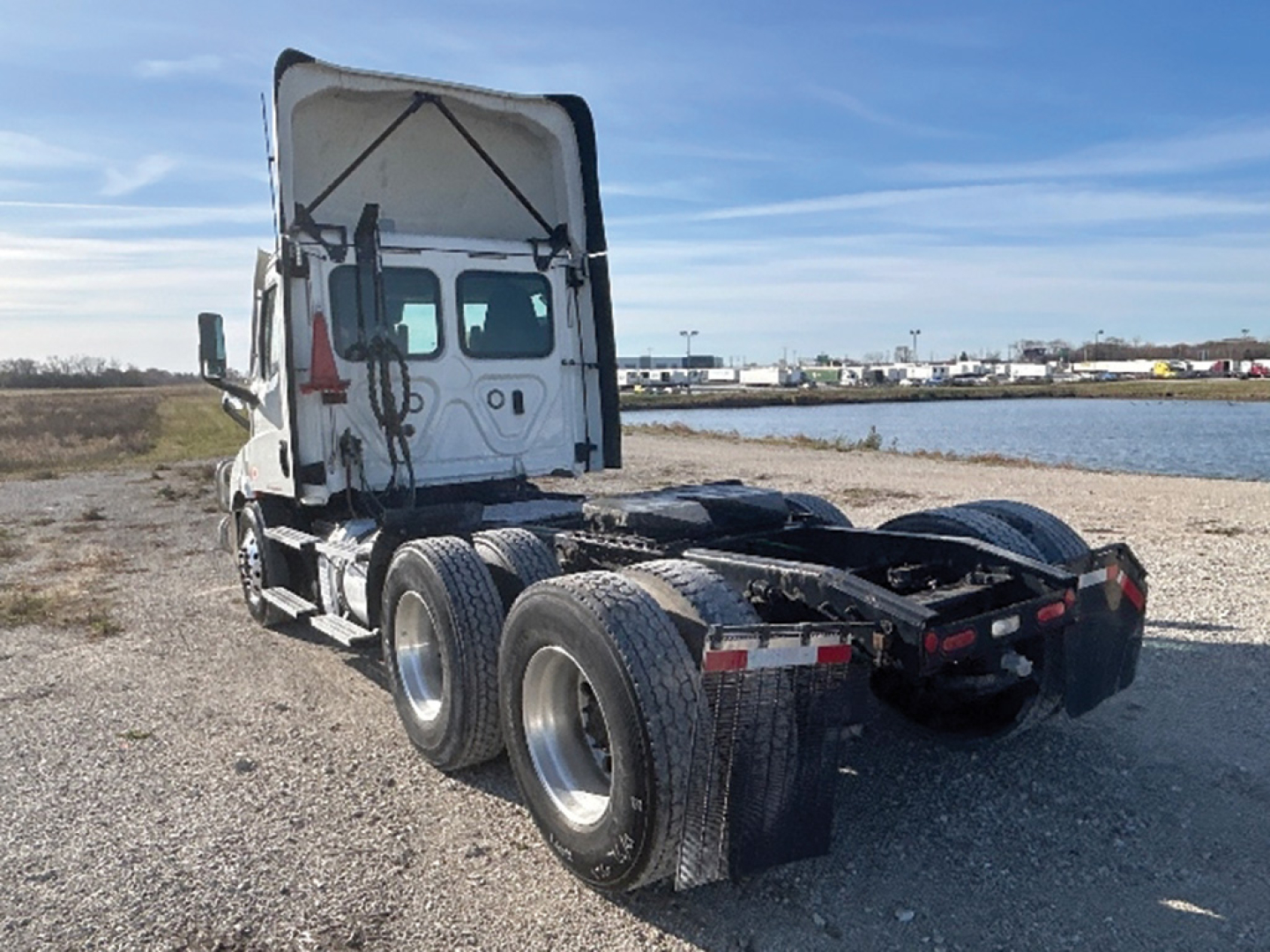 Rear and side view of a Freightliner Cascadia126 tractor truck chassis with fifth wheel missing; dual rear axles; white cab; cargo area open.