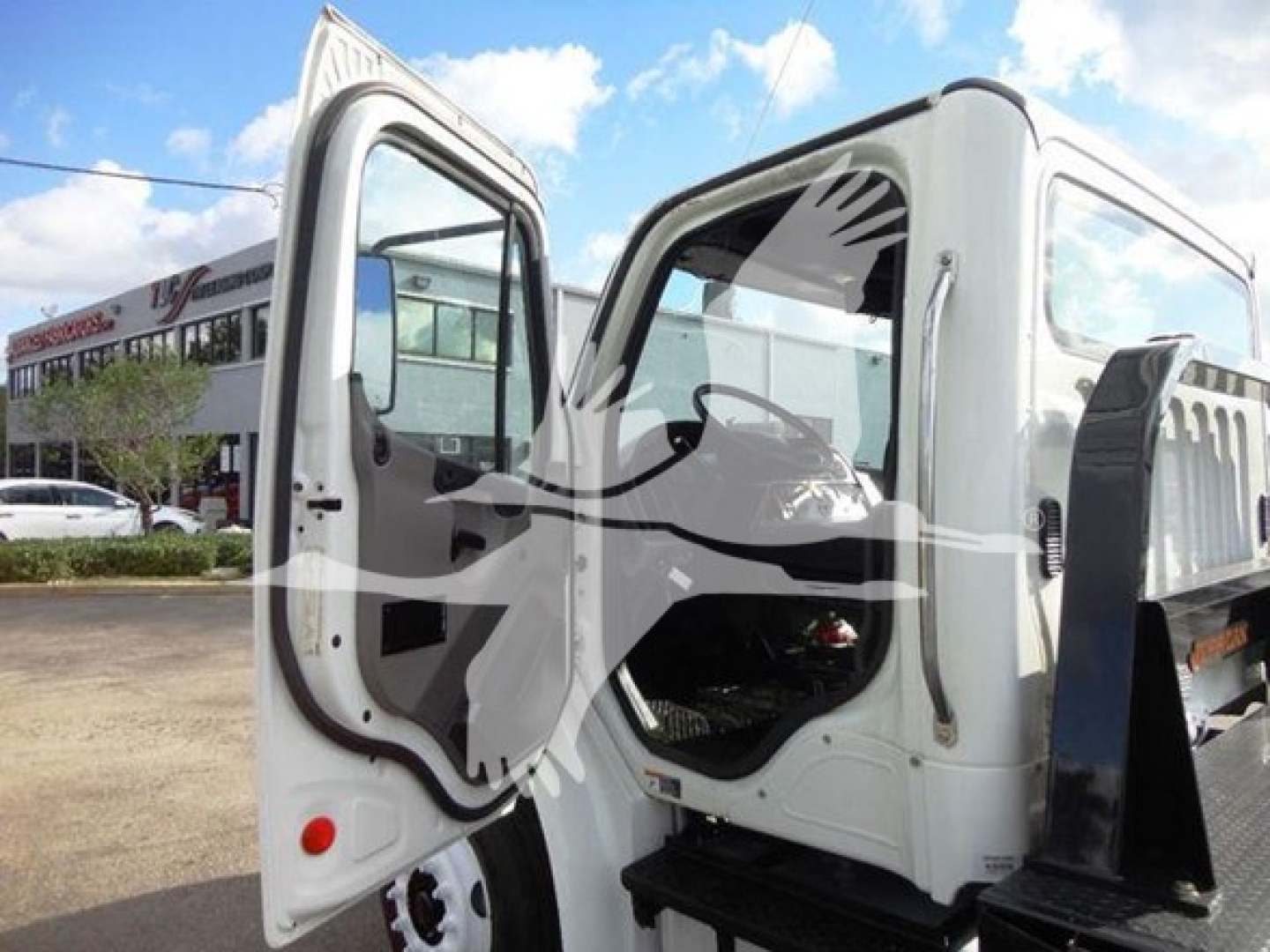Truck cabin of a 2015 Freightliner M2 106 with open doors, showing cab interior and front of flatbed.