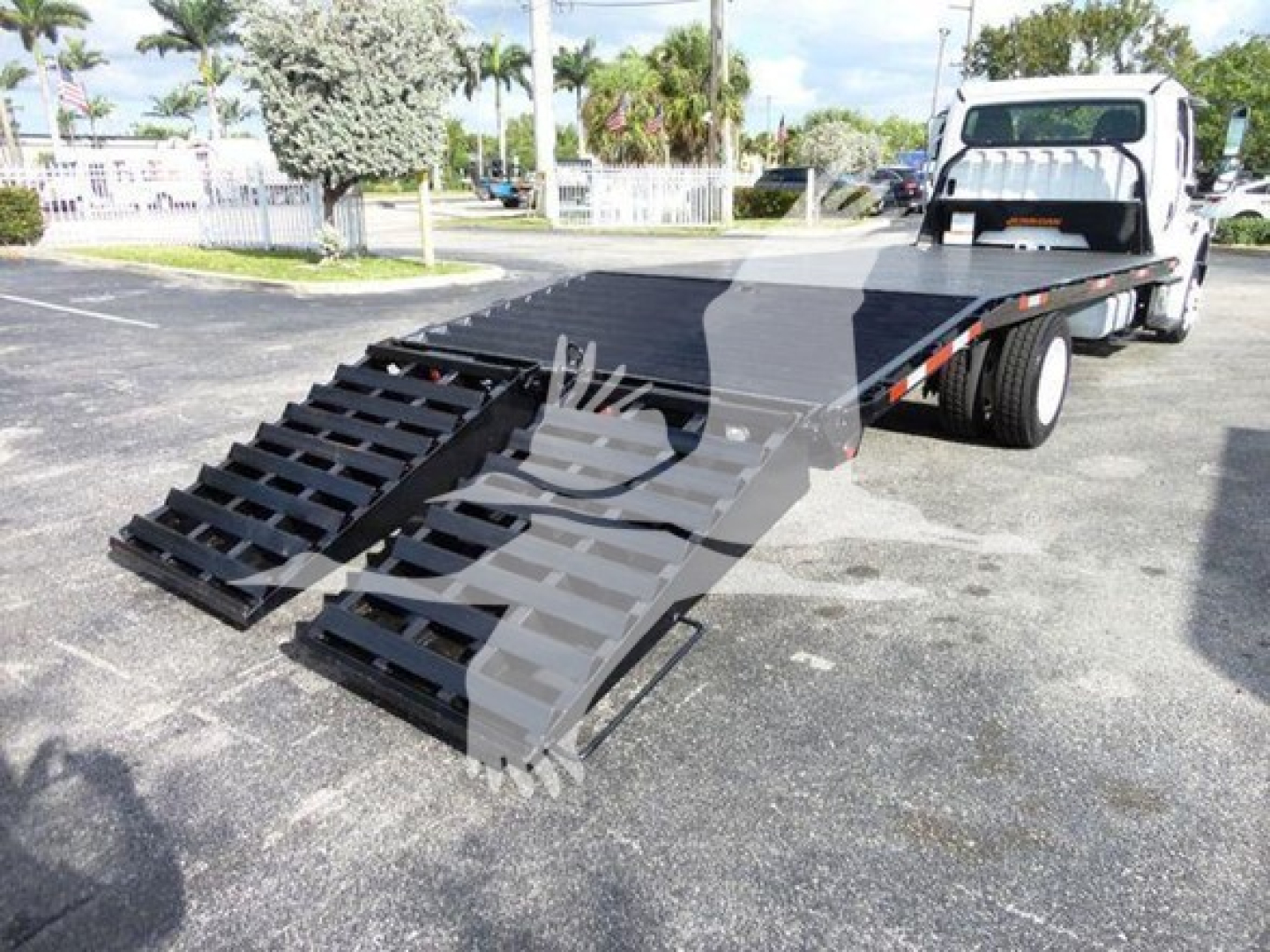 Freightliner M2 106 flatbed tow truck with lowered ramps in front of cab, side view showing flatbed and twin steel ramps.