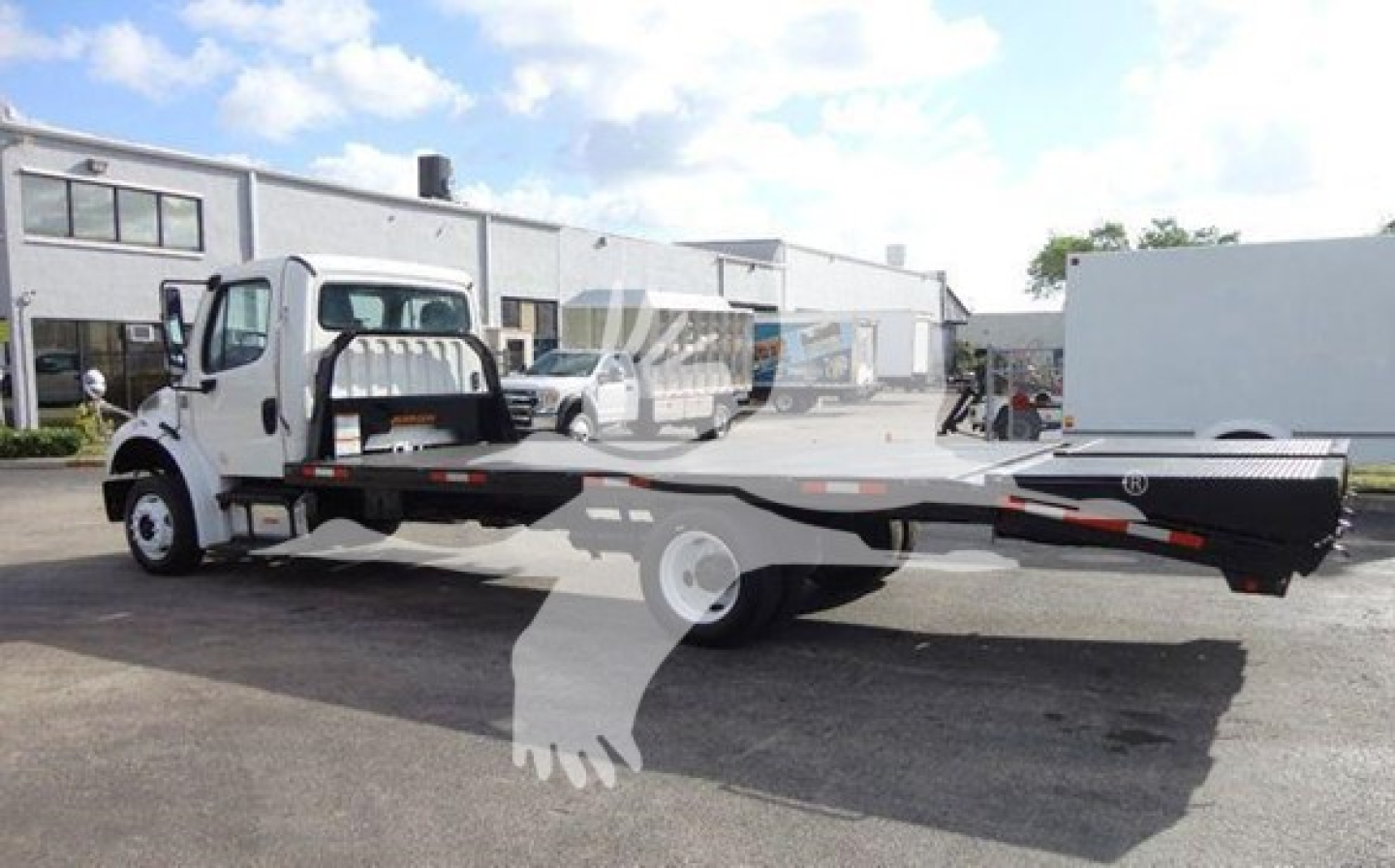 Flatbed tow truck with extended bed on Freightliner M2 106 chassis, white cab, long black steel flatbed, visible in-service condition.