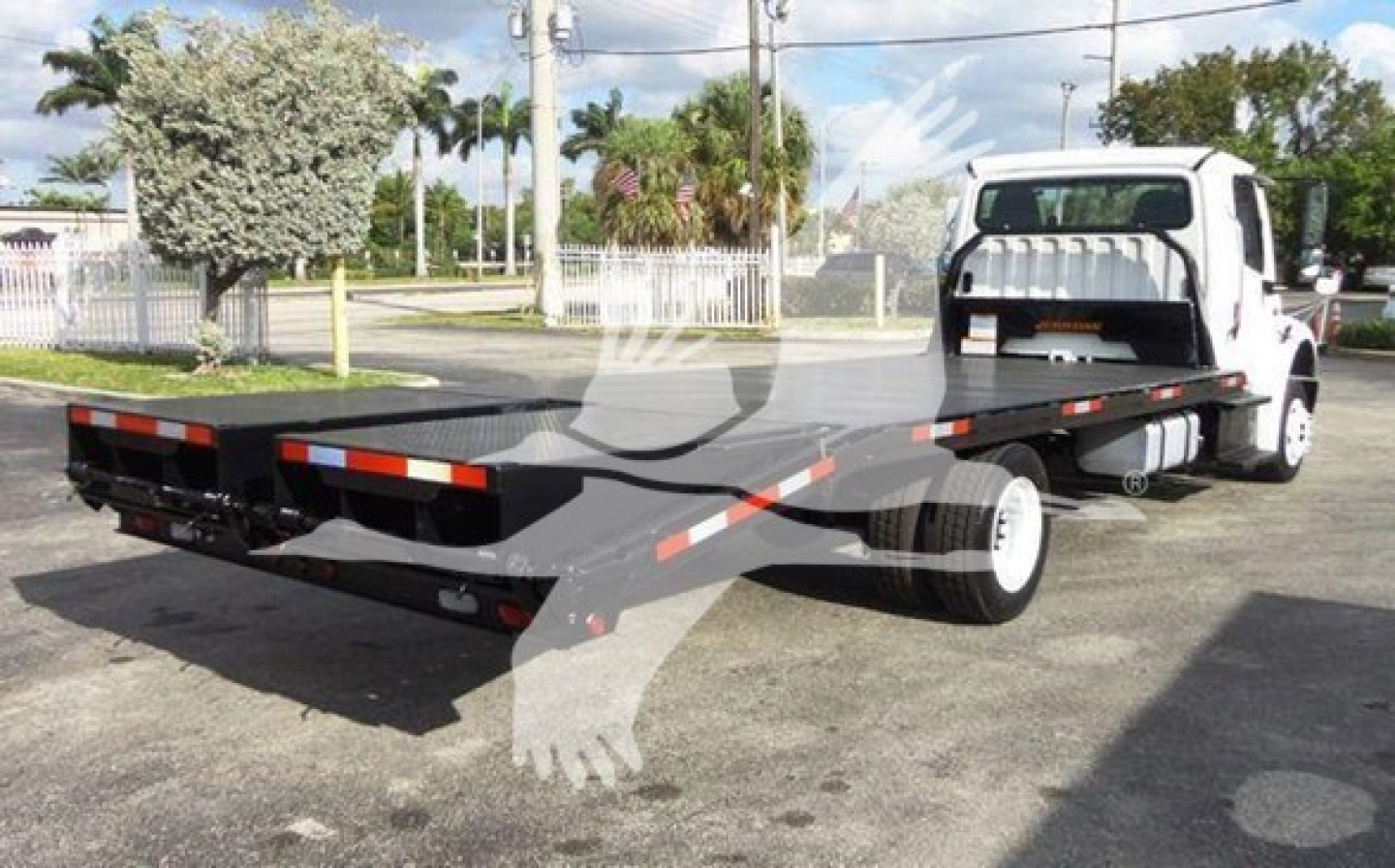 Freightliner M2 106 flatbed truck in yard, rear view showing long flatbed with reflective tape, white cab, VIN 1FVACWDTXFHGR0070 and stock TR0070 visible.