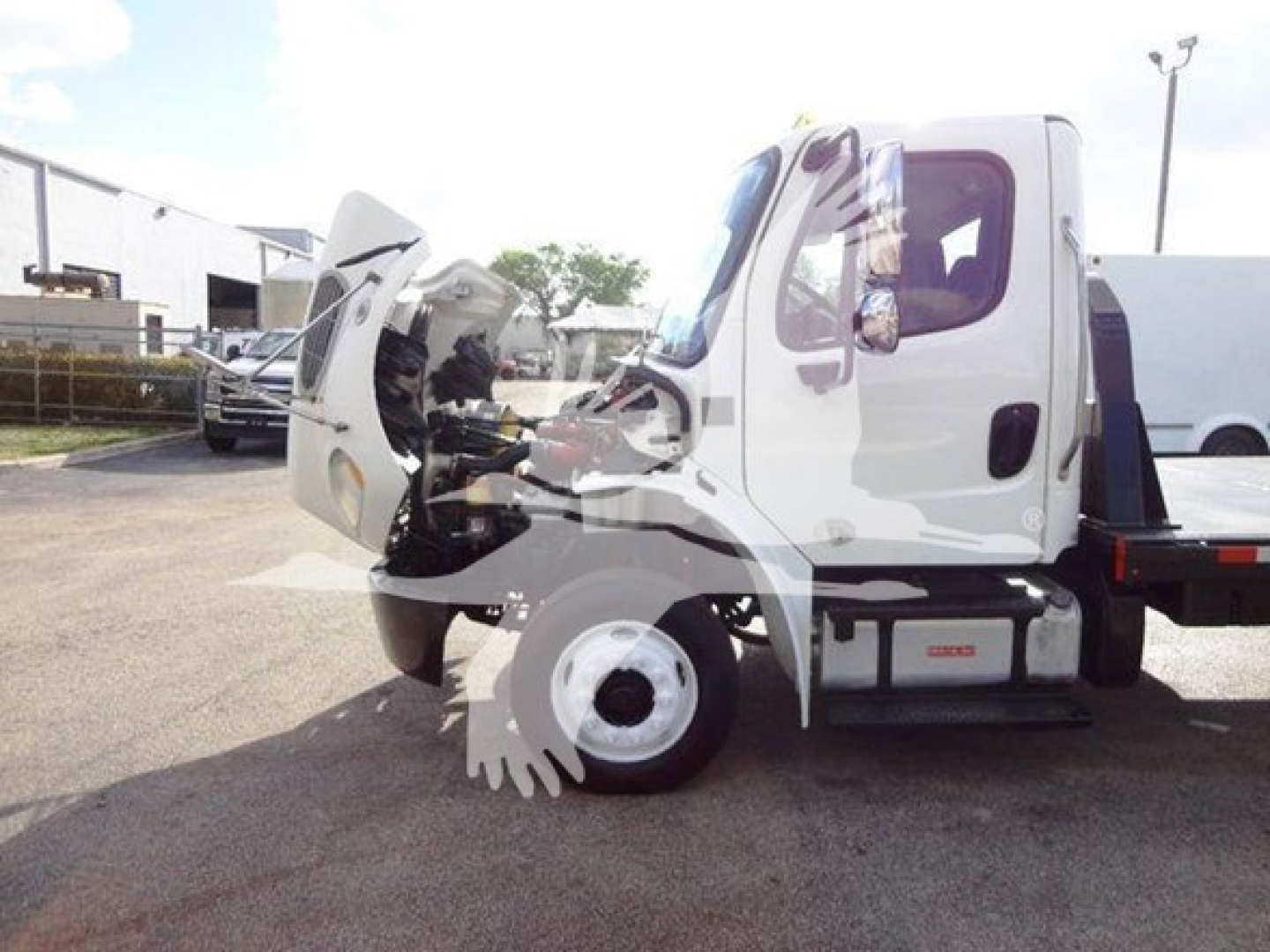 Freightliner M2 106 flatbed truck cab with hood open showing engine bay details.