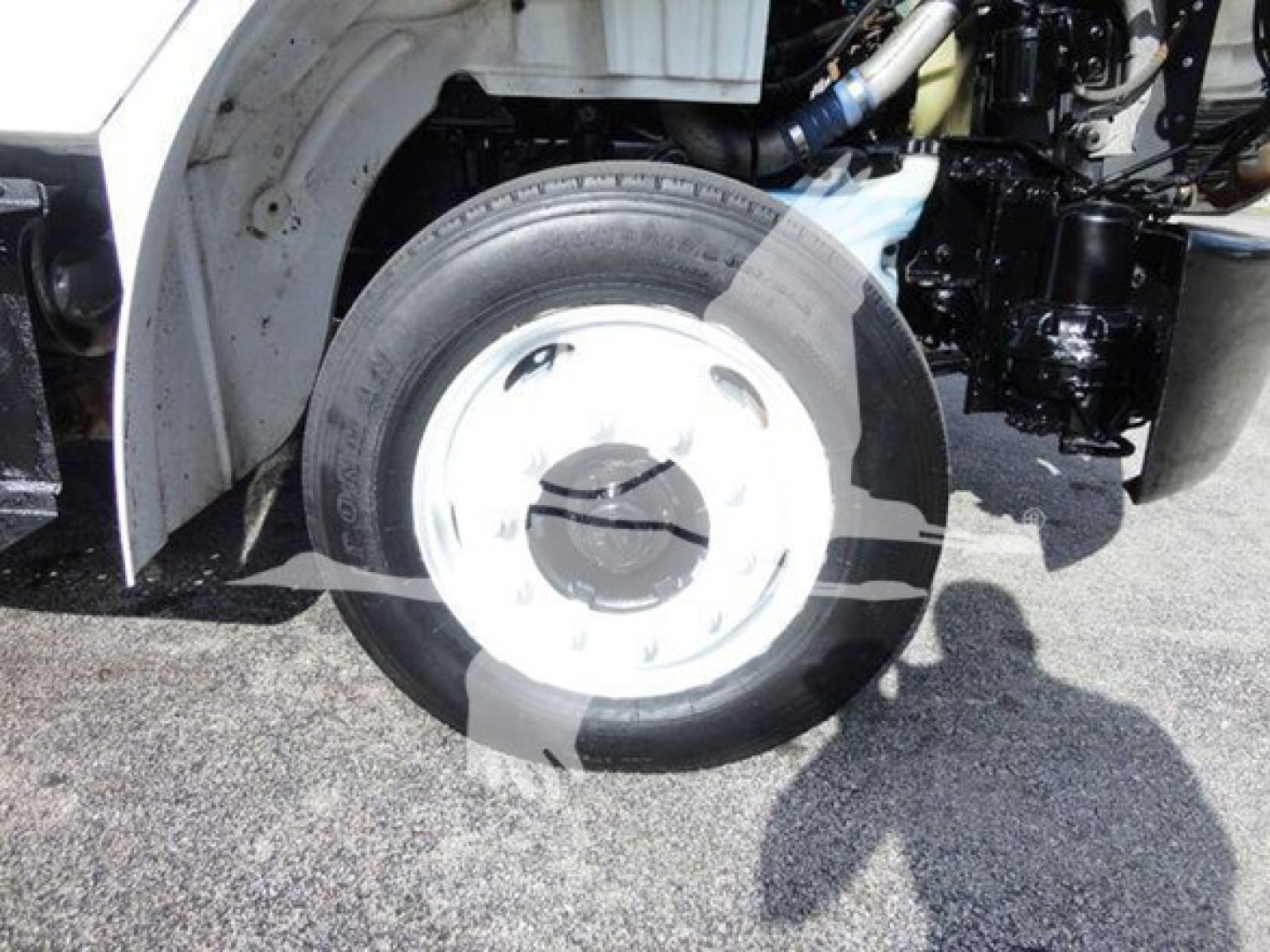 Freightliner M2 106 wheel and front suspension view with white wheel rim and tire, part of flatbed truck chassis visible