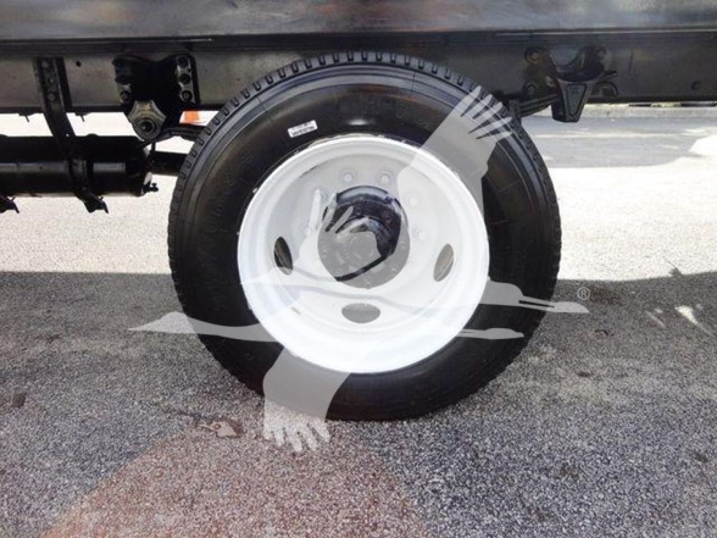 Flatbed truck undercarriage showing wheel and tire with white steel rim and hub area, Freightliner M2 106 identification faintly visible