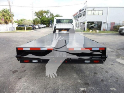 Flatbed truck bed rear view of a 2015 Freightliner M2 106 with a long rectangular flatbed and tail lights, VIN tag area and dealership building in background.