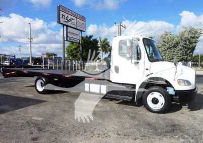 Flatbed tow truck in a dealership lot showing Freightliner M2 106 cab and flatbed chassis.