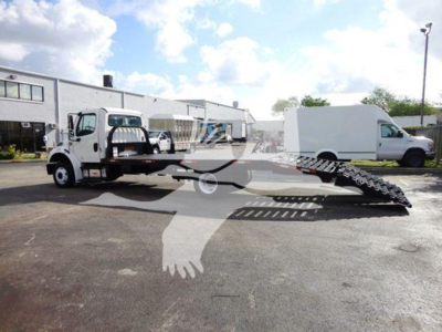 2015 Freightliner M2 106 flatbed tow truck with a lifted wheel-ladder ramp in the bed, side view, white cab, flatbed equipment visible.