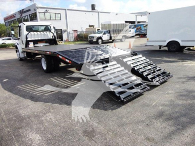 Flatbed tow truck with a ramped loading bed in an outdoor lot; Freightliner M2 106 style flatbed with gooseneck and wheel ramps visible.