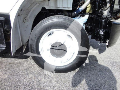 Freightliner M2 106 wheel and front suspension view with white wheel rim and tire, part of flatbed truck chassis visible