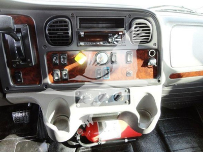 Dashboard of a Freightliner truck showing control switches, wood grain panel, and fire extinguisher mounted under the center console.