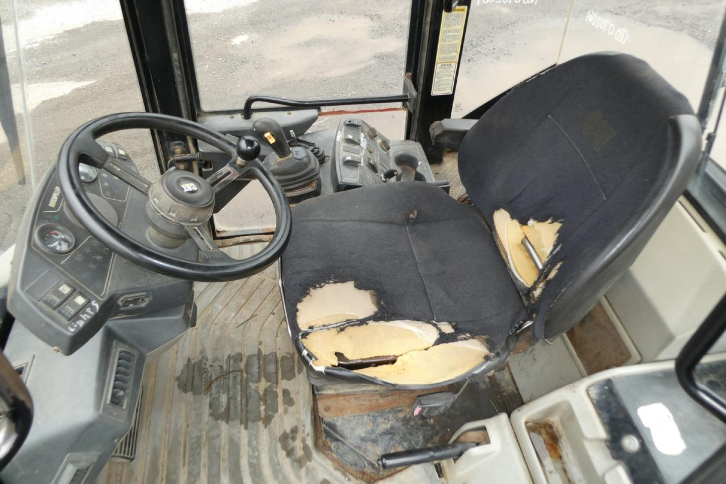 Cab interior of a Caterpillar wheel loader showing a worn driver seat with torn upholstery, steering wheel, and control panel.