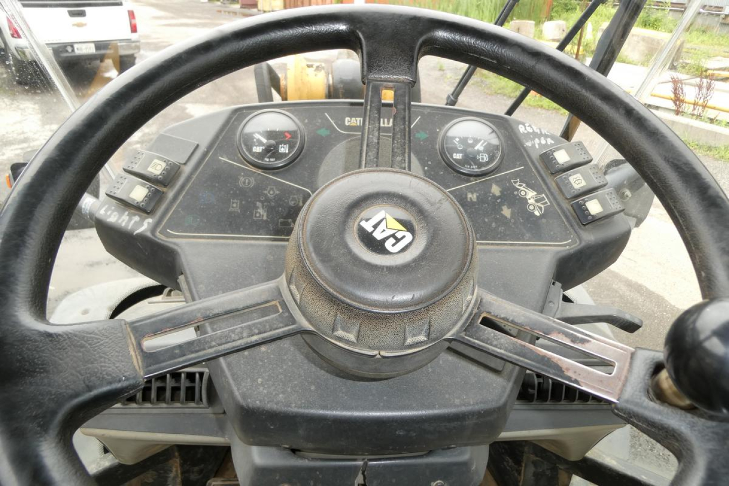 Cab interior of a Caterpillar 902 wheel loader showing steering wheel with CAT logo and instrument gauges.
