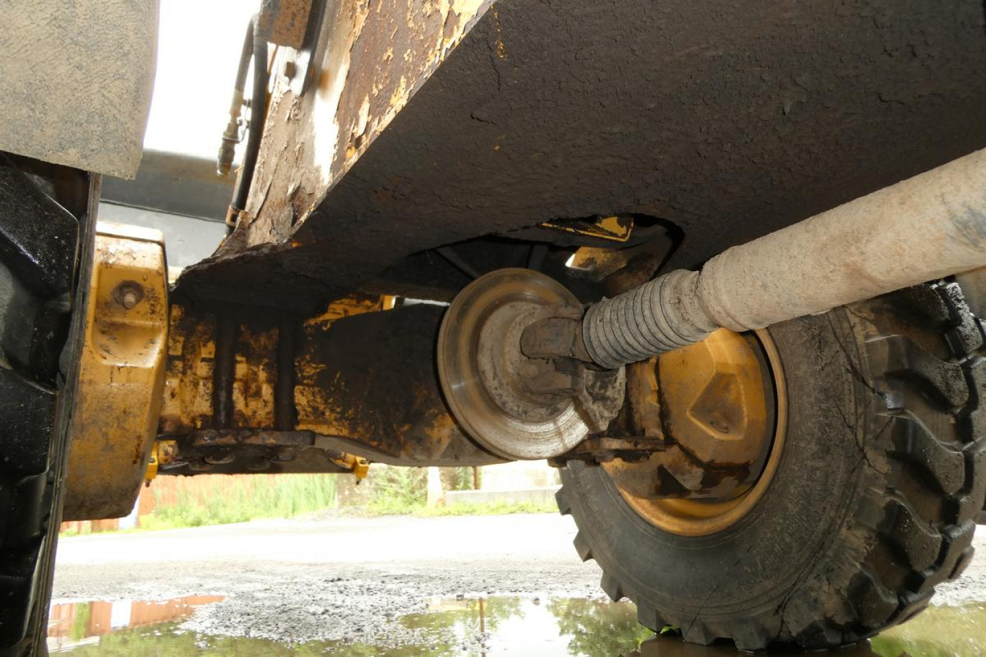 Caterpillar 902 wheel loader undercarriage view showing driveshaft and uneven debris with wheel and tire visible