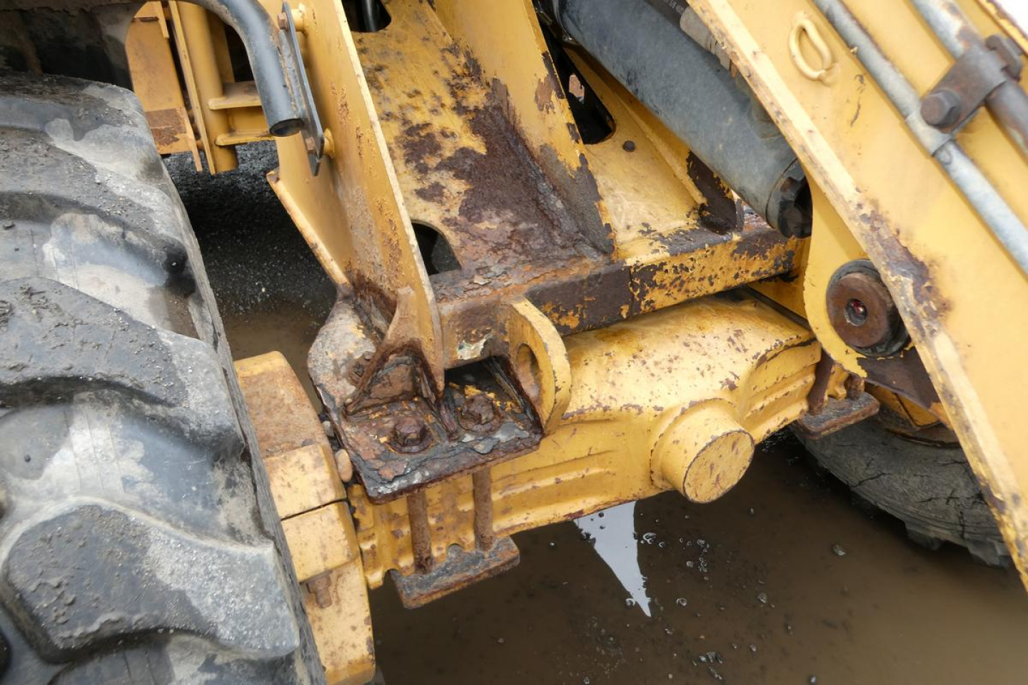 Wheel loader undercarriage with hydraulic pin and yellow painted steel components, CAT logo area, showing wear and hydraulic fittings.