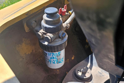 Caterpillar 902 wheel loader fuel filter and hydraulic line close-up showing filter canister with blue handwritten numbers.
