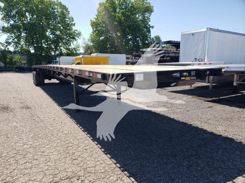 Flatbed trailer rail showing long deck and wheel area with equipment in background.