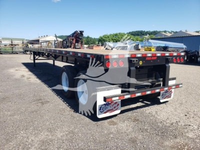 Flatbed trailer showing rear and left side with dual axles, black frame, red and white safety reflectors, mud flaps, and extended ramp area; Steele brand visible on rear bumper.