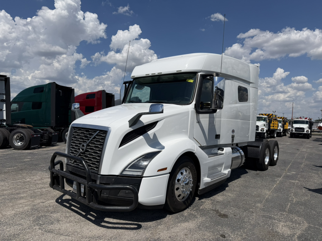 Volvo VNL64T740 2021 white sleeper tractor showing front grille guard and side profile with dual rear axles in a truck lot.
