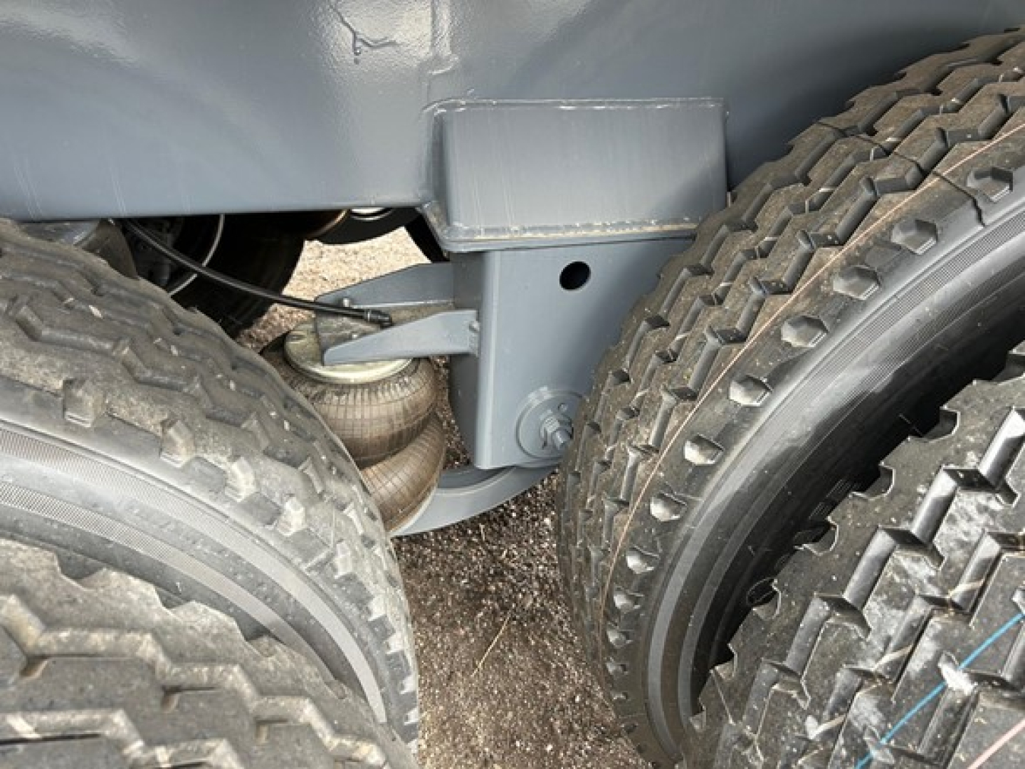 Axle suspension of Dragon Tri Axle Air Ride trailer showing dual tires, air ride suspension components, and frame bracket with coil spring/air bag visible.