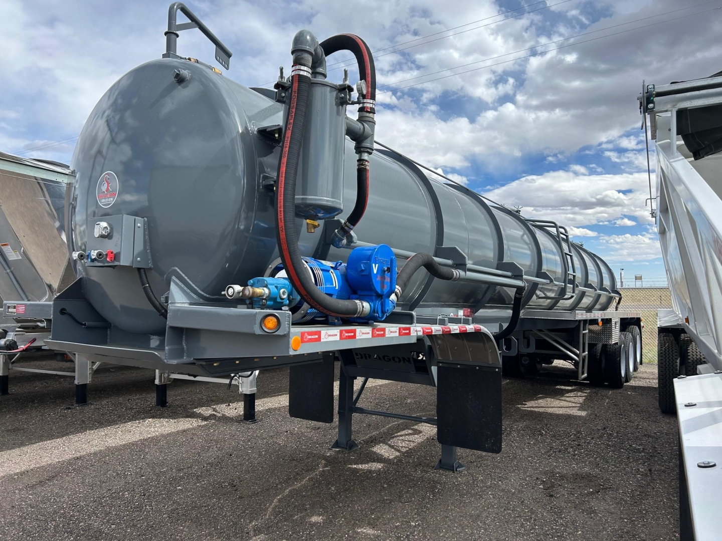 Dragon Vac Tank trailer with cylindrical gray tank, hoses, and blue valve fittings; front end with hitch and support legs visible.