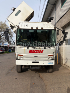 Elgin street sweeper cab front view with logo and elevated hopper on top, white truck with side mirrors and windshield wipers visible.