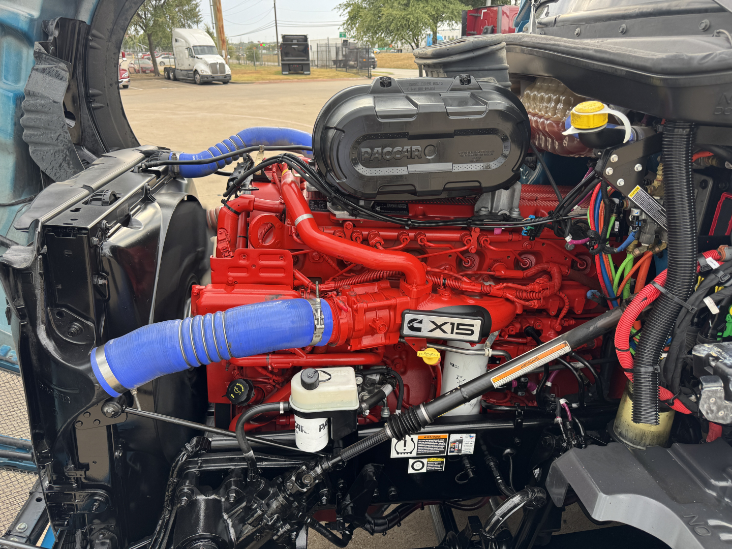 Kenworth T680 engine bay with bright red engine, blue hoses, and black intake, showing label 'X15' on side and various hoses and wiring.