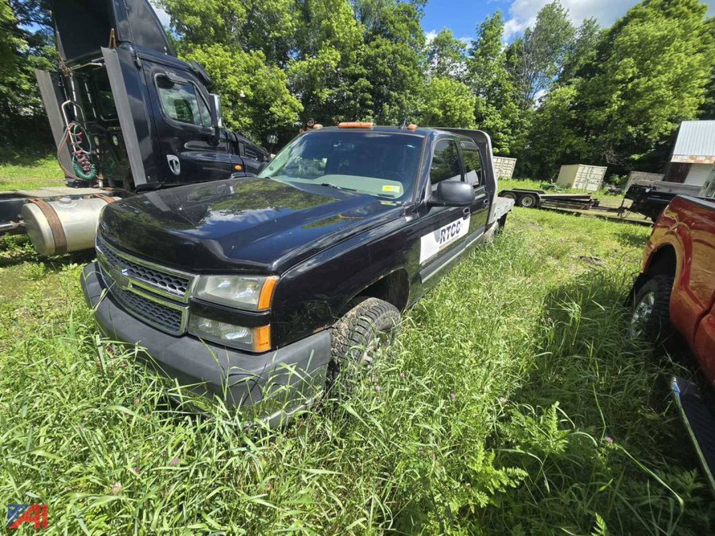 Chevrolet Silverado 2500HD crew cab flatbed truck in overgrown lot, black exterior, orange clearance lights, side step, visible wheels and tires, white pickup on passenger side.