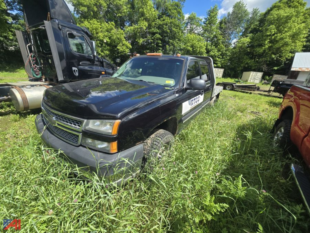 Chevrolet Silverado 2500HD crew cab flatbed truck in overgrown lot, black exterior, orange clearance lights, side step, visible wheels and tires, white pickup on passenger side.