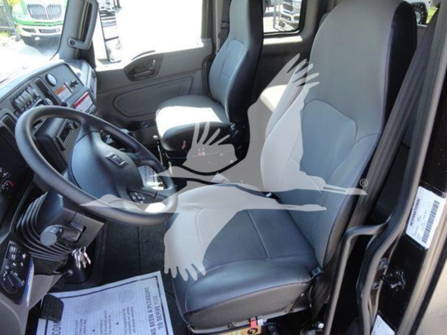 Truck cab interior showing driver's seat and steering wheel with dashboard and passenger seat in view.