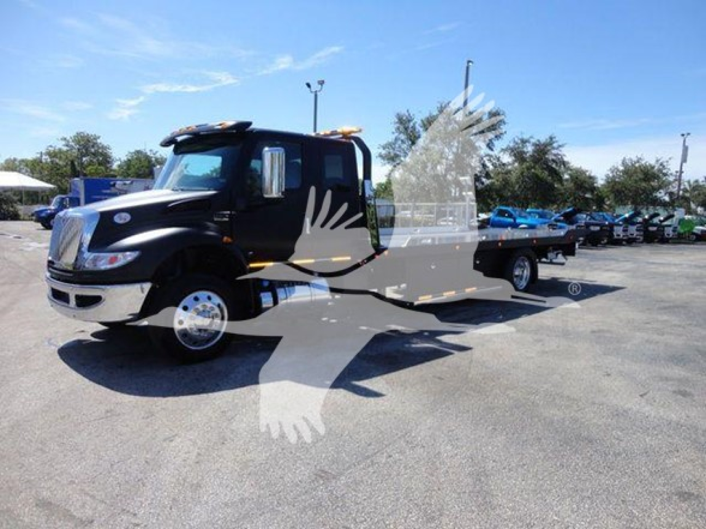 Flatbed tow truck in a dealer lot with a partial watermark, showing International MV cab and flatbed.