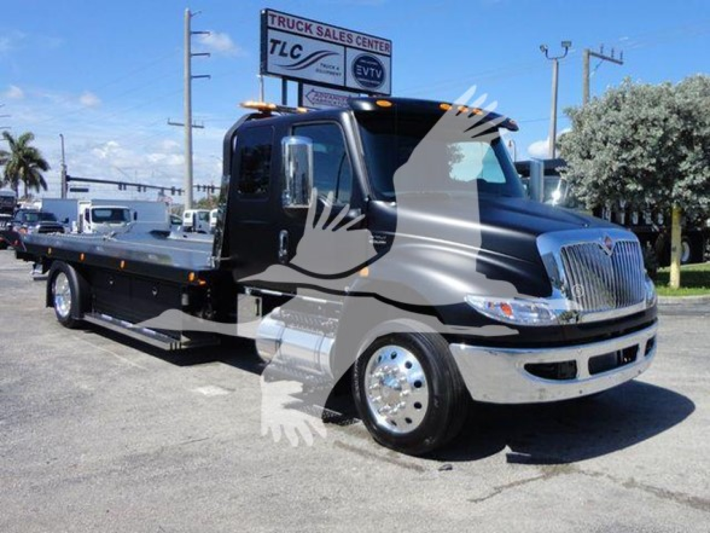 Flatbed tow truck in black and chrome with International badge, showing cab and long flatbed. Text on banner sign in background.