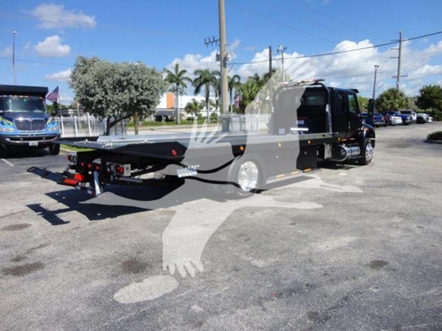 Tow truck with rollback bed in black color, side view, International MV chassis, VIN plate visible, parking lot setting.