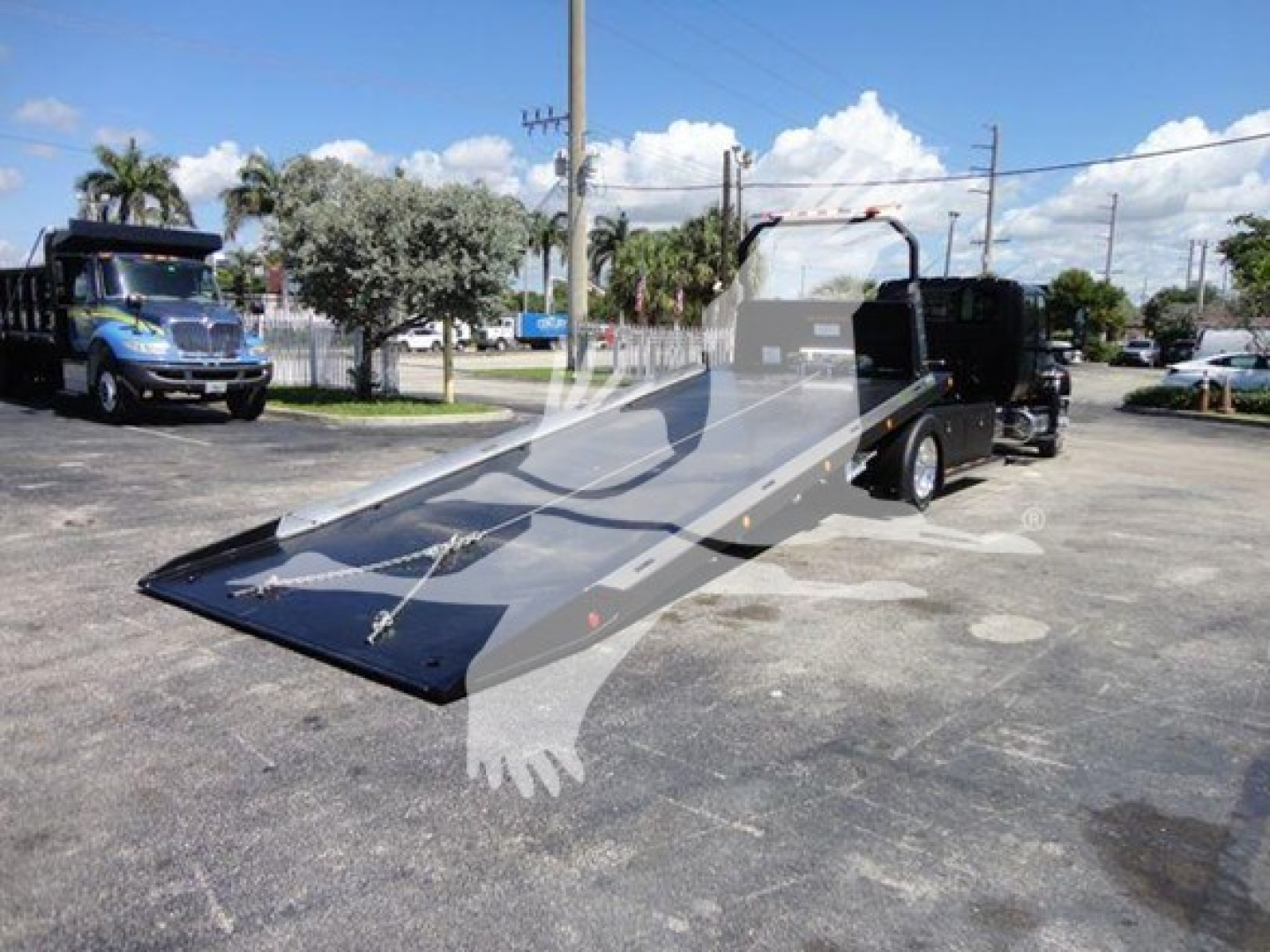 International MV rollback truck with a tilted flatbed viewed from the side, showing hydraulic ramps and towing equipment.