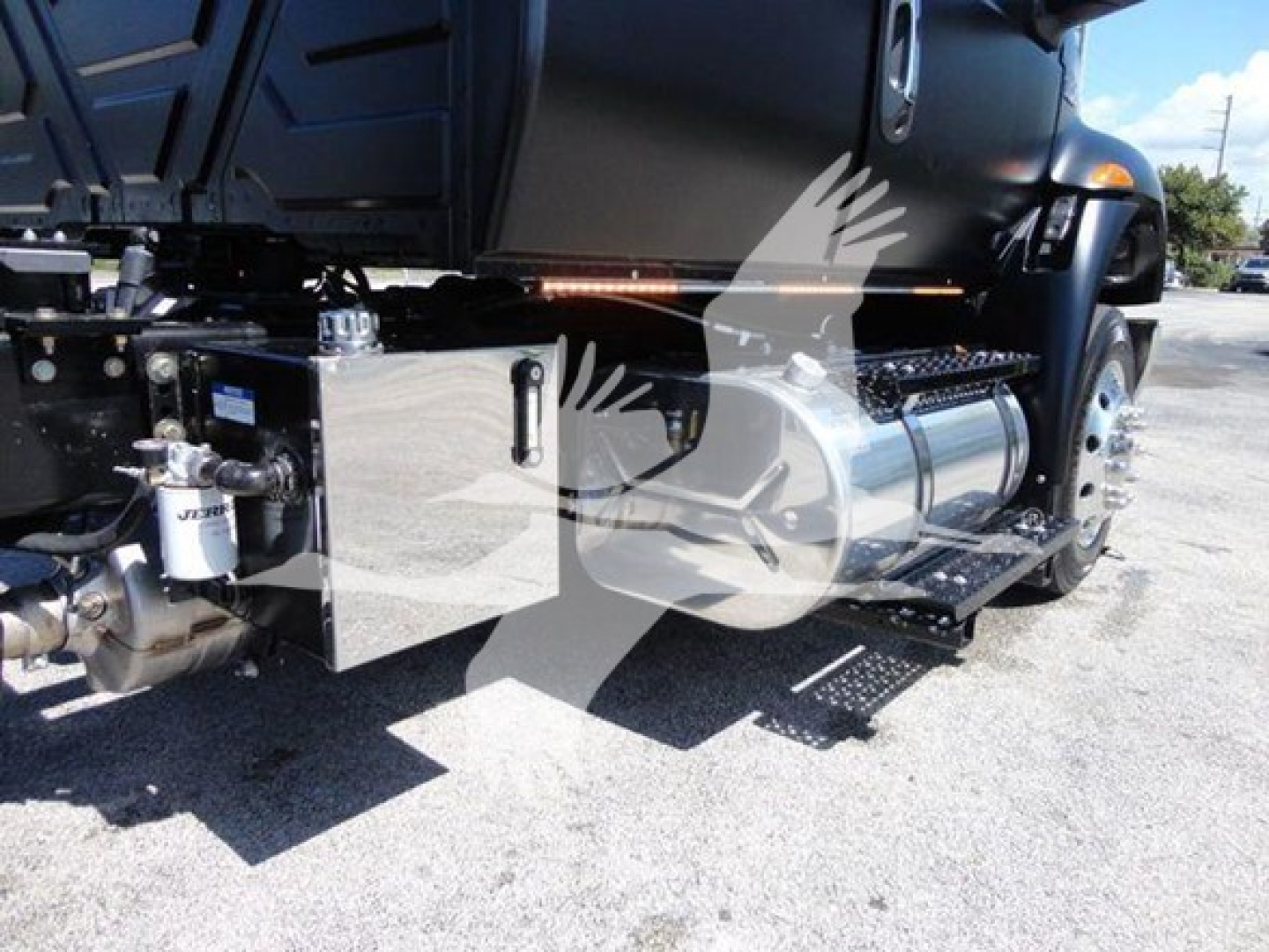 Truck side view showing capability components: metallic toolbox, fuel tank, steps, and hydraulic lines under the cab of a 2022 International MV rollback truck.