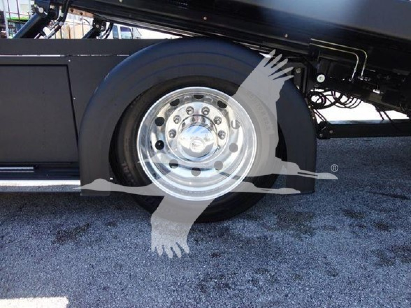 Truck wheel and fender area of a 2022 International MV rollback truck showing polished steel wheel and tire with undercarriage components.