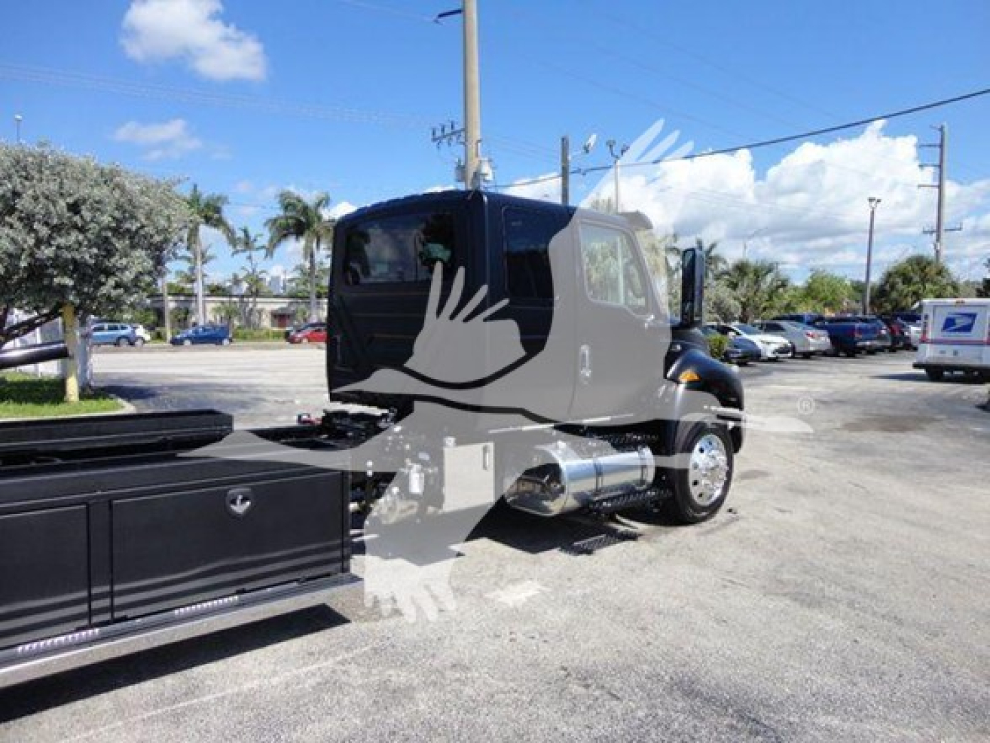 International MV truck cab in a truck yard showing side view, chrome fuel tanks, black sleeper cab, and rollback bed in foreground.
