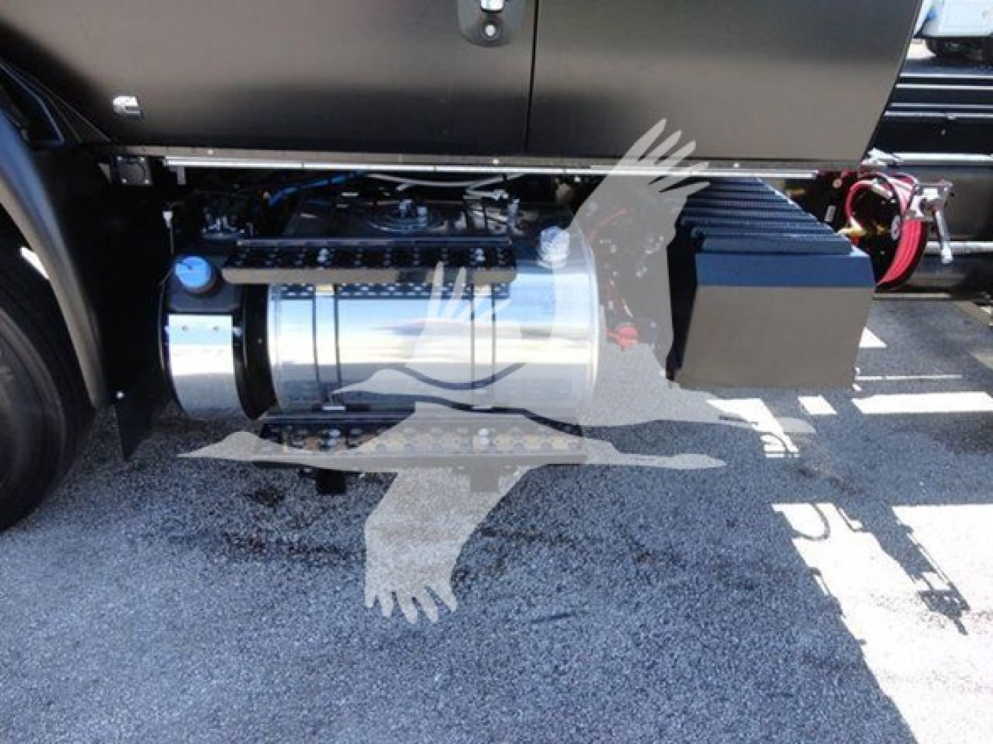 Truck undercarriage showing fuel/air tank and auxiliary equipment beside cab, with a chrome cylindrical tank and black rectangular component.