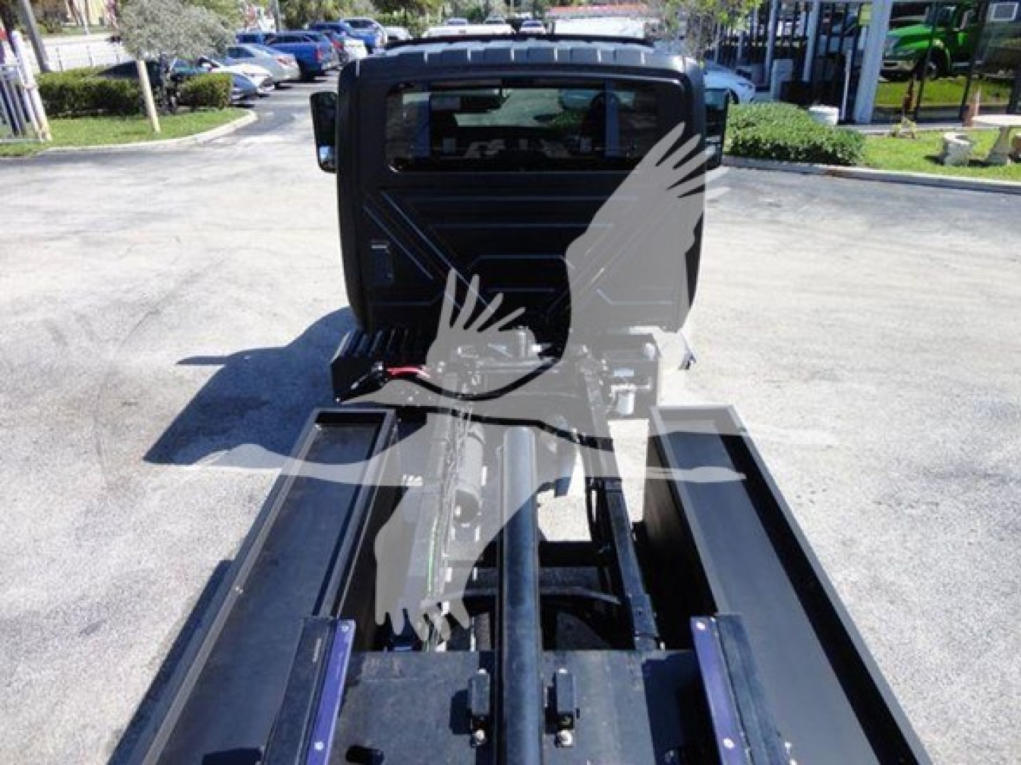 Truck bed with a folded metal platform and hydraulic line visible; faint watermark of a bird logo over center. No legible labels or serial numbers readable.