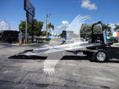 Vehicle side view of a 2022 International MV rollback truck with a lowered flatbed, black chassis, and rear wheel assembly visible.