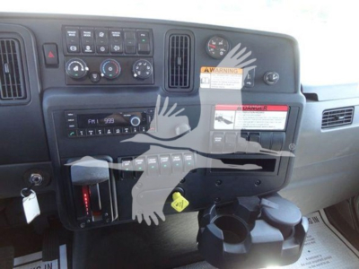 Dashboard of 2022 International MV rollback truck showing controls, gauges, cup holder, and warning stickers; air vents and gear selector area visible.