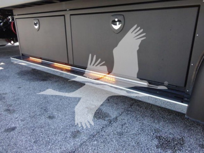 Side view of a 2022 International MV rollback truck showing underbody toolbox and orange ground lighting along the lower door area.