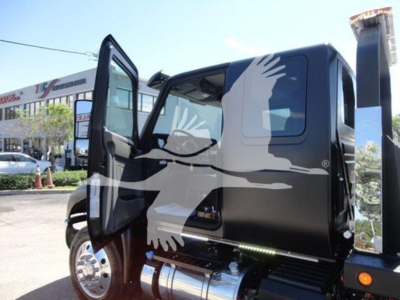 Trucks cab open door showing black International MV rollback truck with chrome fuel tank and side step.