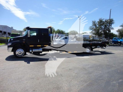 Truck with a rollback bed in a parking lot, side view showing cab and long flatbed.